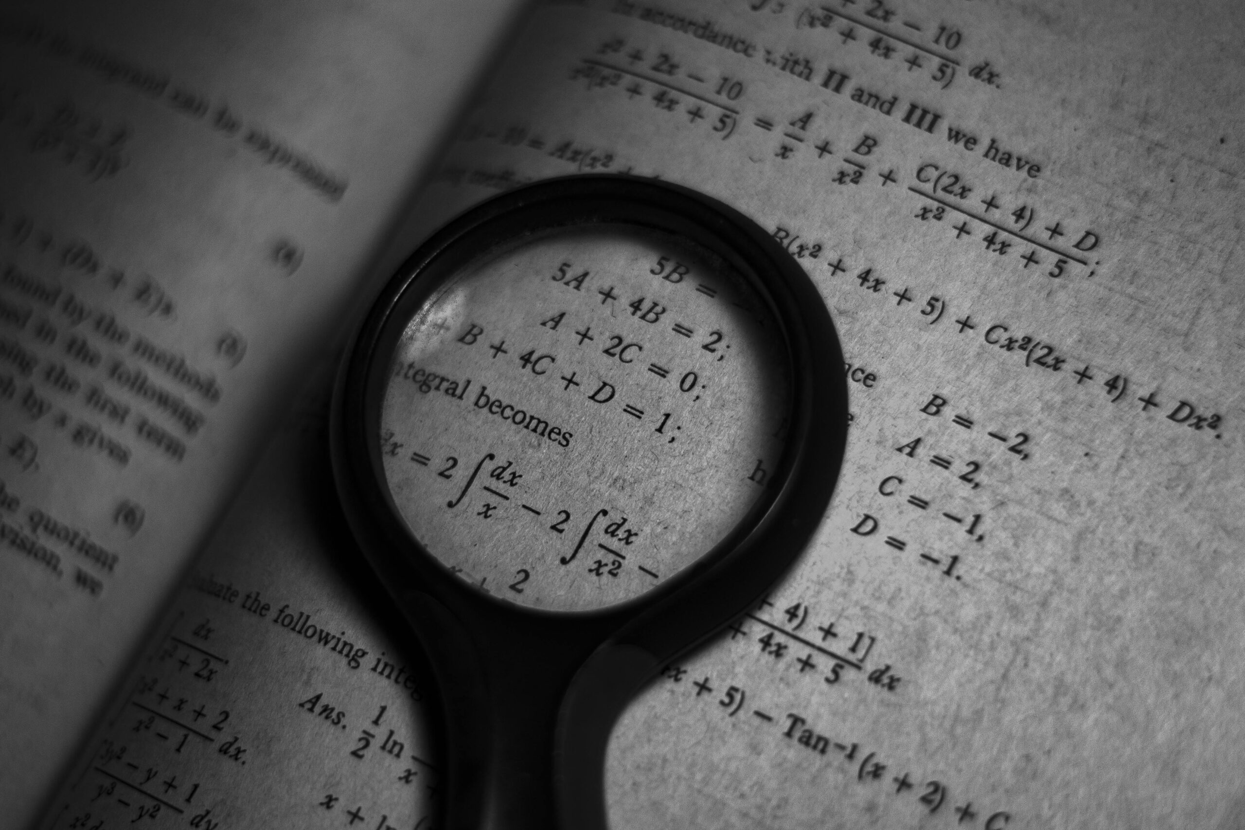 A magnifying glass focuses on mathematics formulas in a book, enhancing study and exploration.